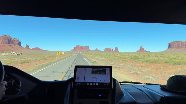 Driver's point of view driving a recreational vehicle towards the iconic buttes of monument valley on a sunny day, using a navigation system on a tablet to reach forrest gump point