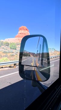 Passenger view from a bus traveling on a scenic highway, with the iconic red rock landscape of monument valley, utah, reflected in the large side mirror on a sunny day