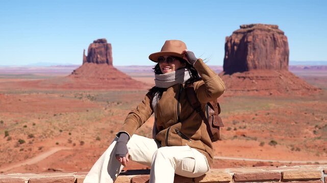 Young smiling adventurer sitting and enjoying the stunning landscape of monument valley, with the iconic sandstone buttes in the background on a sunny day in the american southwest