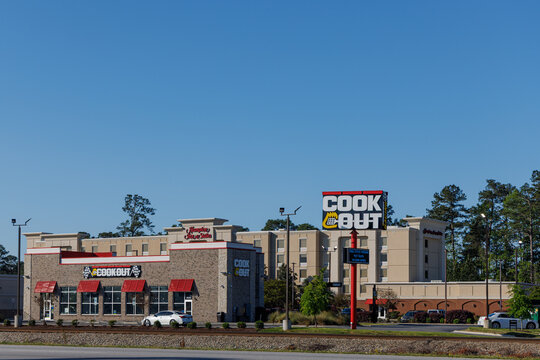 Florence, South Carolina - April 13, 2025: A Cook Out fast-food restaurant with red awnings and large signage stands in front of a Hampton Inn and Suites hotel