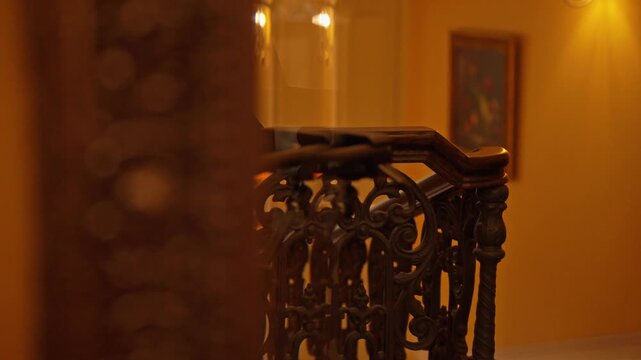 Elegant camera movement revealing a beautiful vintage staircase with a dark wood handrail and ornate wrought iron balusters in a luxurious, warmly lit home interior with soft focus