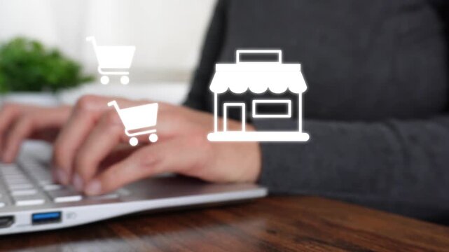 Close-up of a woman's hand working on a computer while pointing at an animated store icon with a pair of shopping carts.