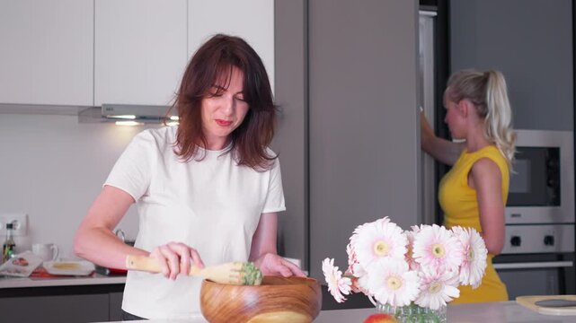 Friends gather in a modern kitchen, joyfully cooking and sharing moments. One stirs a delicious dish while the other prepares in the background, creating a lively atmosphere.
