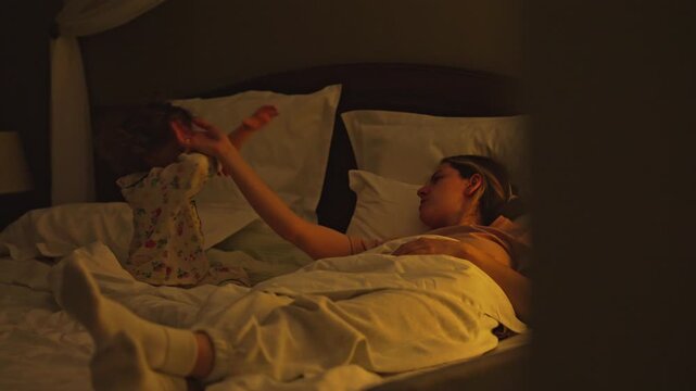 Loving mother and her young daughter spending quality time together before sleep, playing a hand clapping game in a cozy, dimly lit bedroom, creating a warm, heartfelt family memory