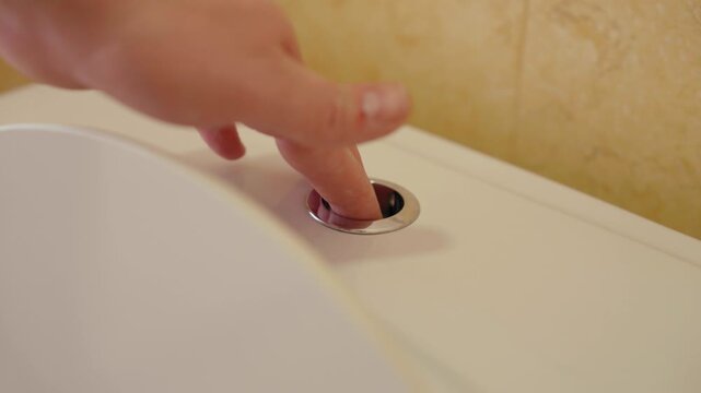 Close up of a child's hand pressing the half flush button on a modern dual flush toilet, showcasing the concept of water conservation and teaching hygiene habits to children