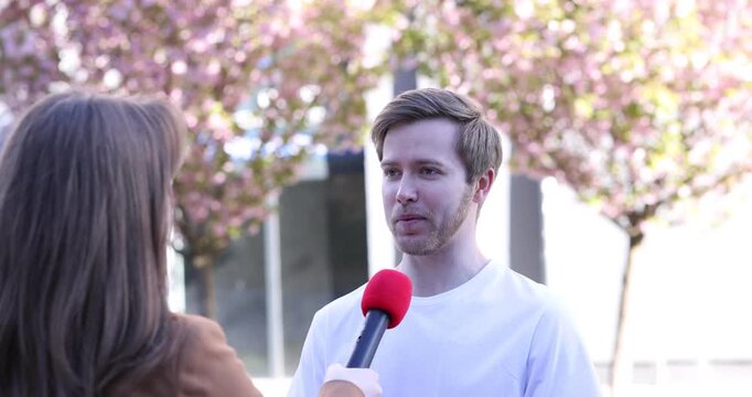 Professional journalist with microphone interviewing man outdoors
