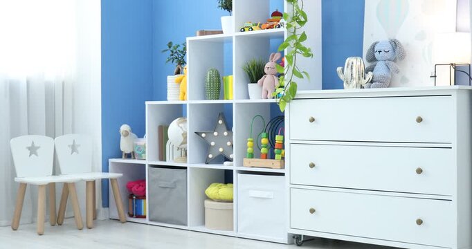 Shelving unit with different toys and decor near blue wall in child's room. Interior design