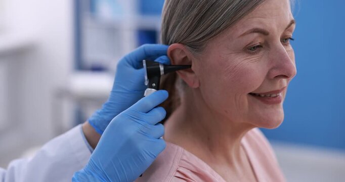 Hearing test. Doctor examining woman's ear with otoscope in clinic, closeup