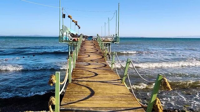 Perspective View of a Rustic Wooden Pier with Rope Railings Overlooking the Wavy Blue Sea and Horizon. Sunny Summer Day at Sarkoy Beach, Tekirdag, Marmara Region, Turkey.