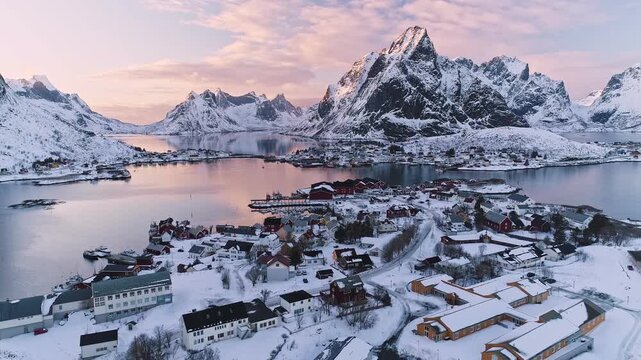 Aerial view of the snowy fishing village of Reine in Lofoten with red cabins and majestic mountains at sunset Reine, Nordland, Norway.