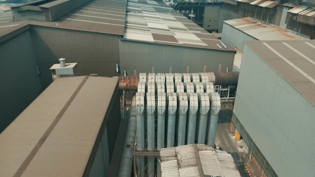 Cinematic aerial top-down tilt up revealing a large industrial factory complex with ventilation pipes and urban city skyline background.