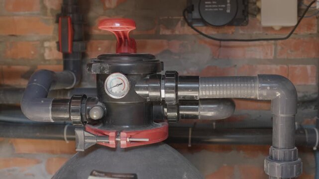 Person turning valve on pool sand filter system in pump room for maintenance and cleaning.