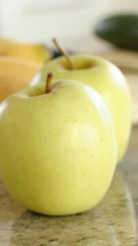 Vertical video: Moving camera framing two yellow green apples on stone counter, sharpening focus