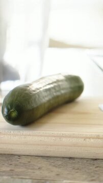 Vertical video: Pulling back camera revealing cucumber on cutting board by kitchen window, glass