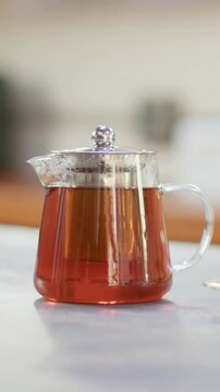 Vertical video: Shifting camera showing glass teapot sitting on kitchen counter, to reveal saucer