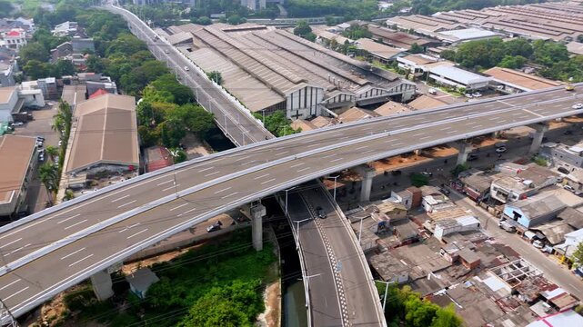 Vibrant aerial side movement of an elevated highway bridge next to high voltage electricity towers in an industrial area.