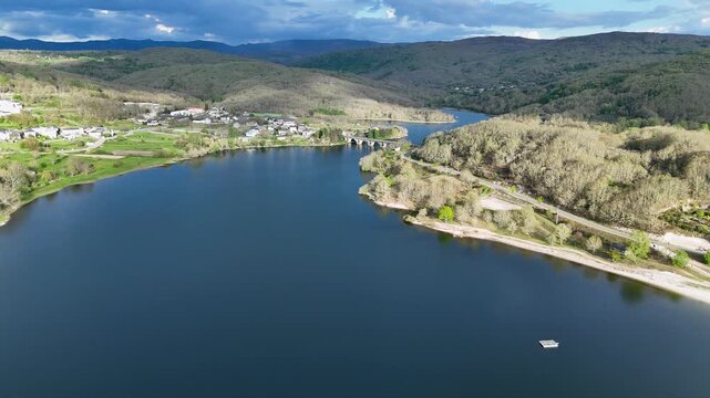 Aerial view of Encoro de Prada reservoir with its bridge and the surrounding green hills and village in A Veiga, Ourense, Spain.
