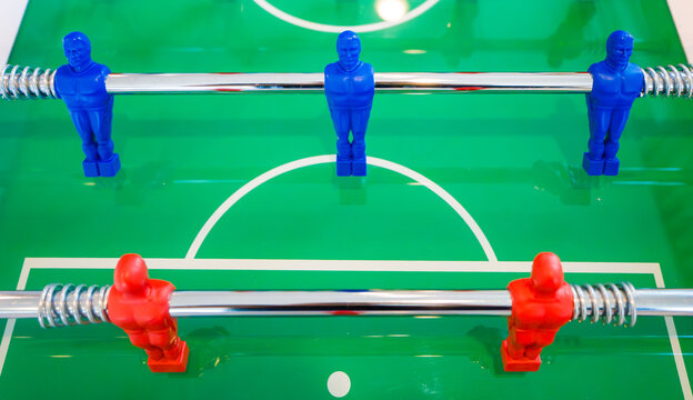 Close frontal view of blue and red plastic team figures mounted on metal rods over a green foosball table game playing field.