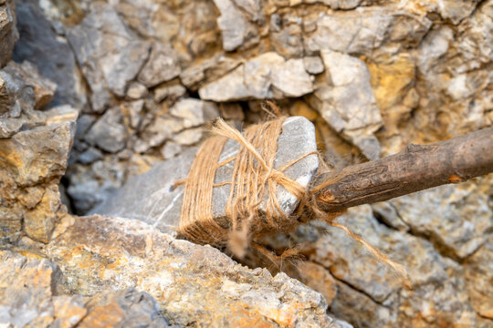 Handmade primitive stone spear with jute rope binding on wooden stick wedged into rough rocky surface, ancient weapon, survival concept.
