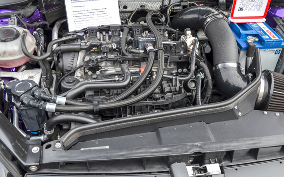 Complex engine bay of modified car features aftermarket APR components, large cold air intake, and braided hoses. Spec sheet indicate it is performance build on display