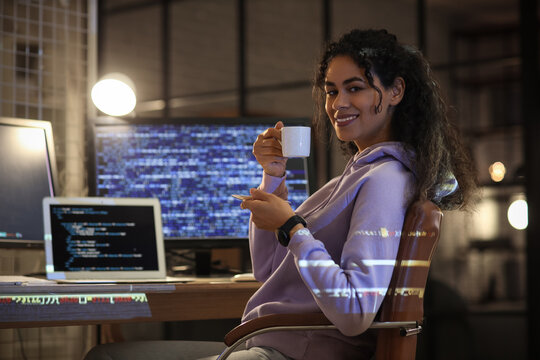Female African-American programmer with coffee cup working in office at night