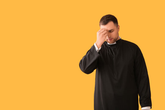 Young priest cross oneself on yellow background