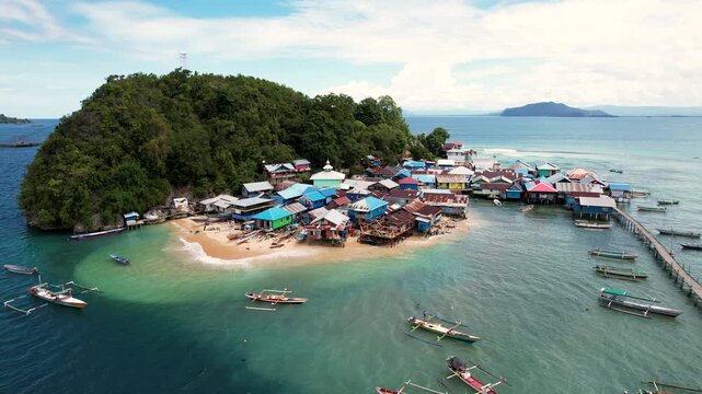 Aerial view of a coastal village with colorful houses on stilts, a sandy beach, and traditional boats in turquoise water, Jayapura, Papua, Indonesia.