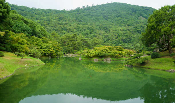 Wide panoramic view of a scenic pond and lush green mountains at Ritsurin Garden in Takamatsu, Japan