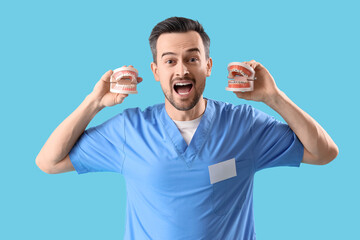 Naklejka premium Portrait of funny male dentist with jaw models on blue background