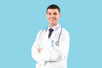 Fototapeta premium Male doctor with blue ribbon on color background. Prostate cancer awareness concept