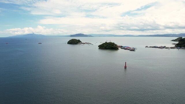 Aerial view of lush tropical islands and a red navigation buoy in the calm waters of the bay with distant mountains under a cloudy sky Jayapura, Papua, Indonesia.
