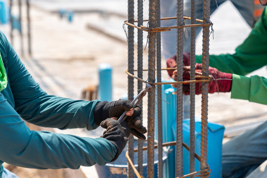 Close-up of construction workers' hands using pliers to secure steel rebar with tie wire for a concrete pillar.