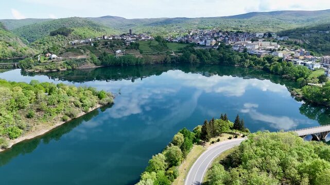 Aerial view of the historic town of Viana do Bolo overlooking the calm reservoir with cloud reflections and lush green hills Viana do Bolo, Province of Ourense, Spain.