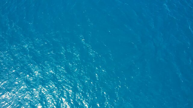 Aerial view of deep blue sea water with gentle ripples and sunlight reflections in Paralia Ofriniou, Greece.