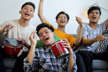 Obraz premium Group of Joyful Asian Men Playing Drums and Cheering While Watching Live Sports Match