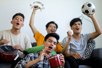Obraz premium Group of Four Enthusiastic Asian Men Celebrating Sports Victory with Drums and Soccer Ball