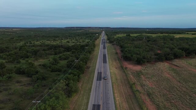 Aerial Drone View of Empty Rural Country Highway Road Surrounded By Grassy Fields and Green Trees With Blue Sky