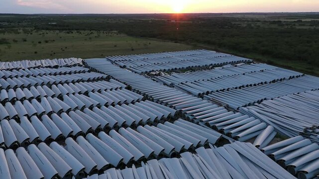 Aerial Drone View of Rows of Wind Turbine Blades Stacked Together in Green Agricultural Field in Rural Town at Dusk Sunset