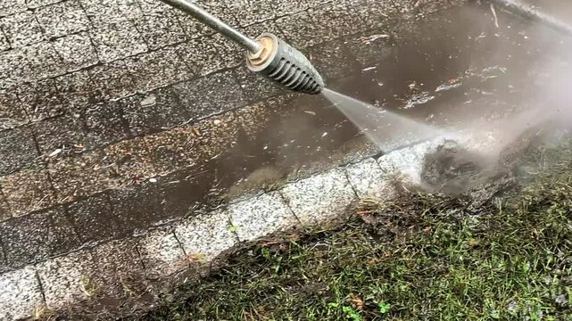 Close-up of a high-pressure water jet cleaning dirty granite paving stones with a turbo nozzle. Professional power washing service removing dirt and moss from a driveway, satisfying industrial motion.
