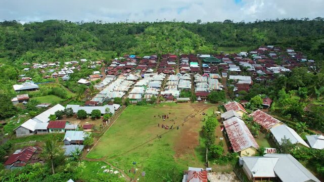 Aerial drone footage of Baturotok village, in Sumbawa regency, Sumbawa island, Indonesia, with many local houses, colorful roofs, a wide grass football field and school, with children