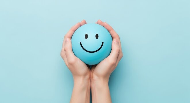 Hands holding a blue ball with a smiling face on a light blue background