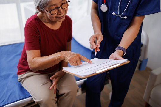 Senior asian woman consulting with nurse, discussing medical checklist and treatment plan, understanding healthcare information, making informed decisions on health insurance forms at clinic