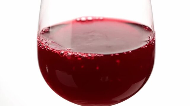 Extreme close-up of rich red wine pouring into a glass, creating dynamic ripples and splashes against a high-key white background. high-speed detail of alcoholic beverage.