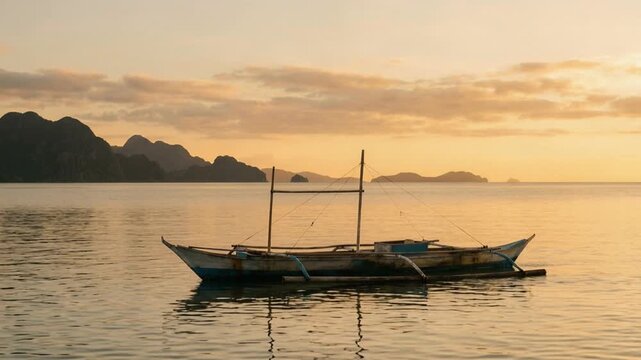 small filipino outrigger boat floating on calm water sunset