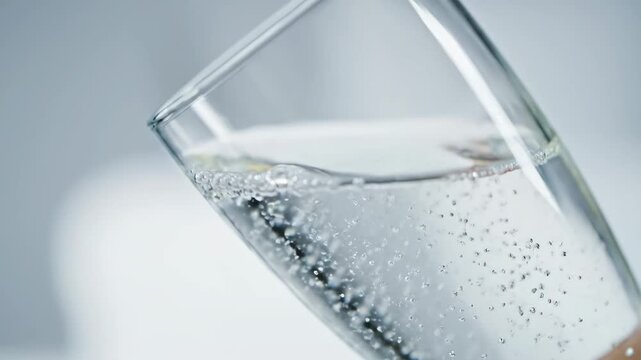 Close up of highly carbonated sparkling water being poured into a tilted glass, showing rapid rising bubbles and fizzing effervescence for refreshment
