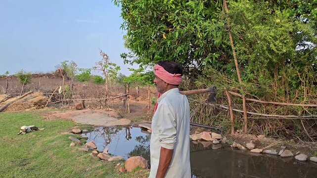 Indian farmer standing in a village field holding an axe on his shoulder