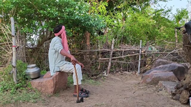 Indian villager sitting on stone, holding axe and looking thoughtful