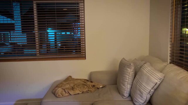 Interior establishing shot of a coastal apartment in Redondo Beach with open window blinds revealing a softly illuminated exterior bathed in cool blue light. The foreground shows a lived-in room.