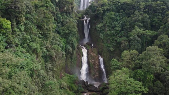 Aerial view of Curug Klenting Kuning waterfall cascading down rocky cliffs surrounded by lush tropical rainforest in Kecamatan Limbangan, Central Java, Indonesia.