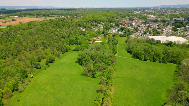 A cinematic drone shot capturing the vibrant greenery of rolling hills and open fields. The bright daylight highlights the natural textures of the landscape, creating a peaceful and scenic rural atmos